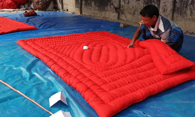 Man inspecting a bright red quilted mattress pad laid on a blue tarp in a workshop setting.