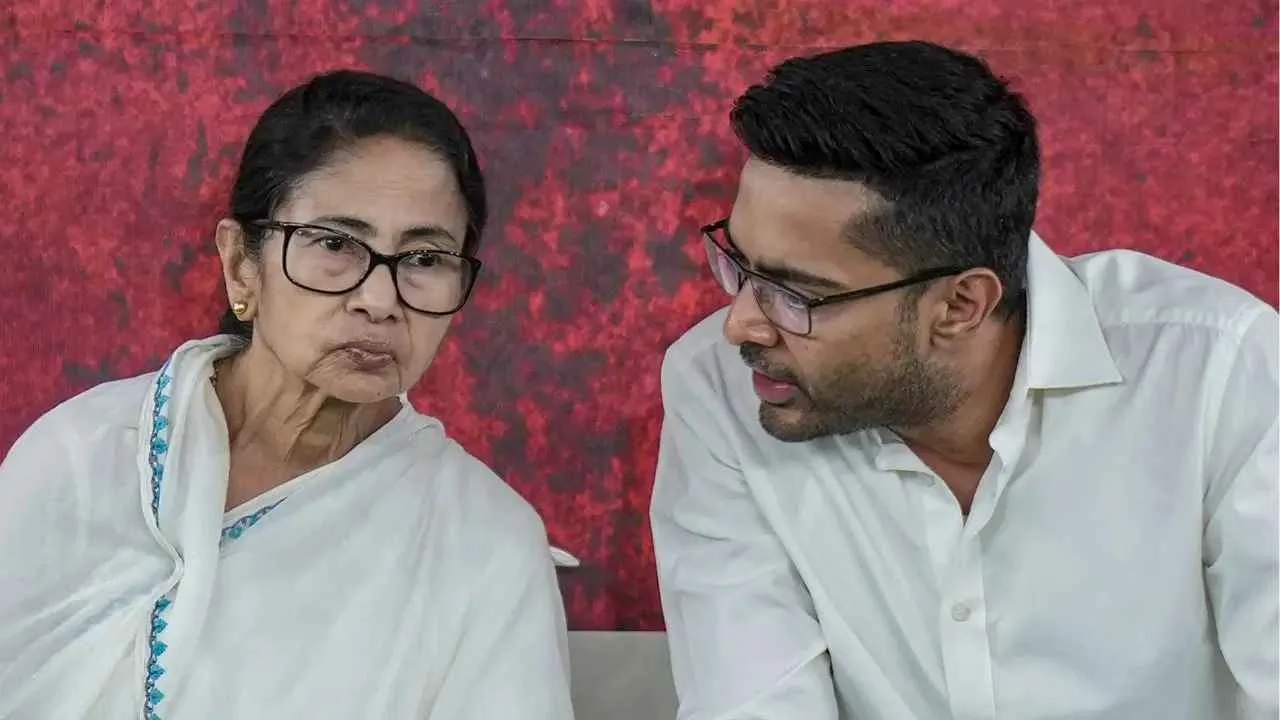 Elderly woman with glasses in a white shawl sits beside a man in a white shirt, both looking at each other against a red textured backdrop.