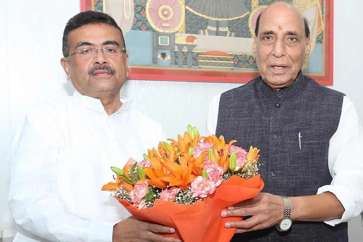 Two Indian men pose indoors, holding a bouquet of orange lilies and pink carnations wrapped in orange paper.