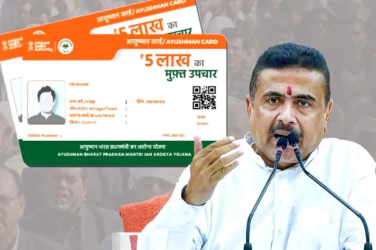 Person at a microphone speaking, with a large Ayushman Bharat health insurance card displayed in the background
