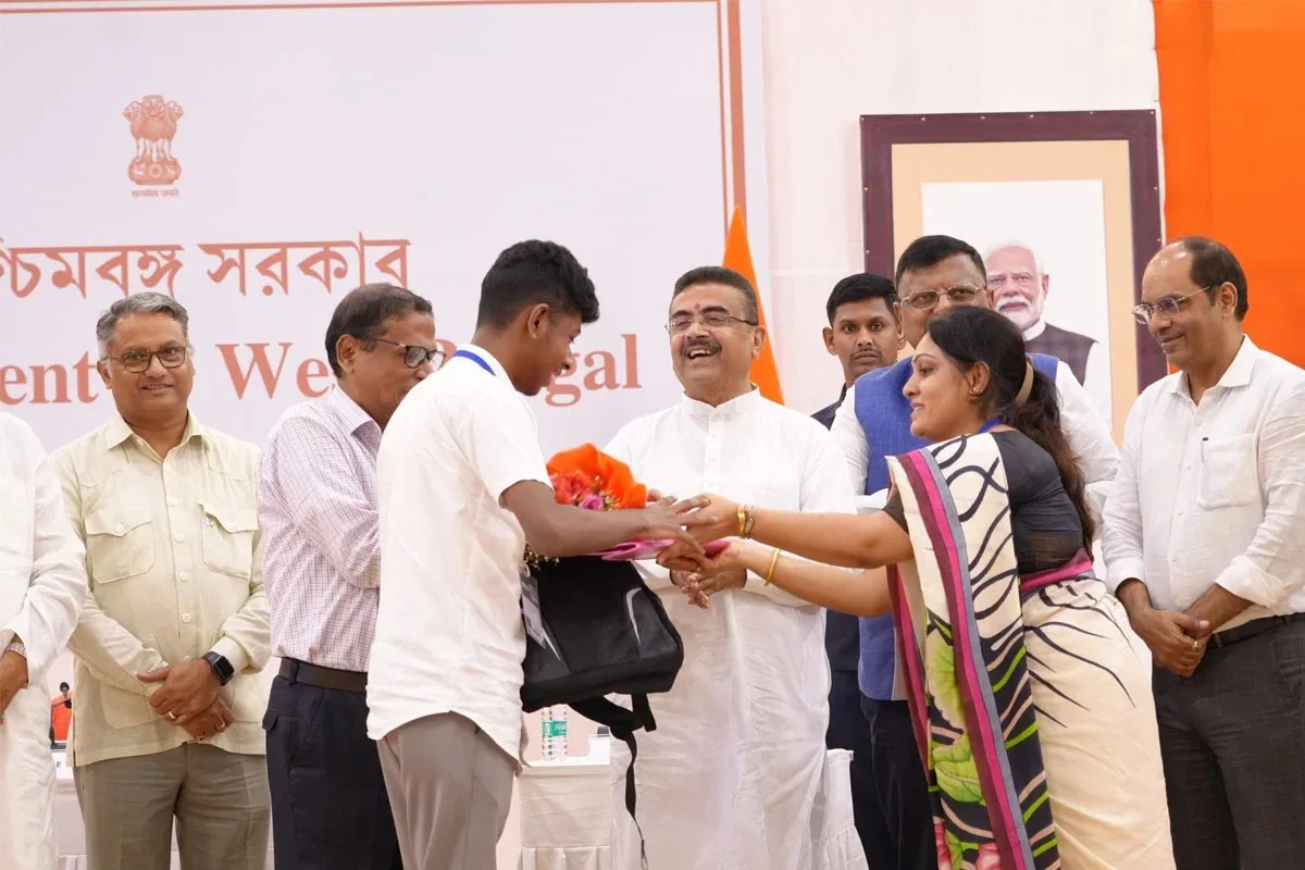 Student receives a bouquet from a man in a white shirt during a government ceremony as officials look on from the stage.