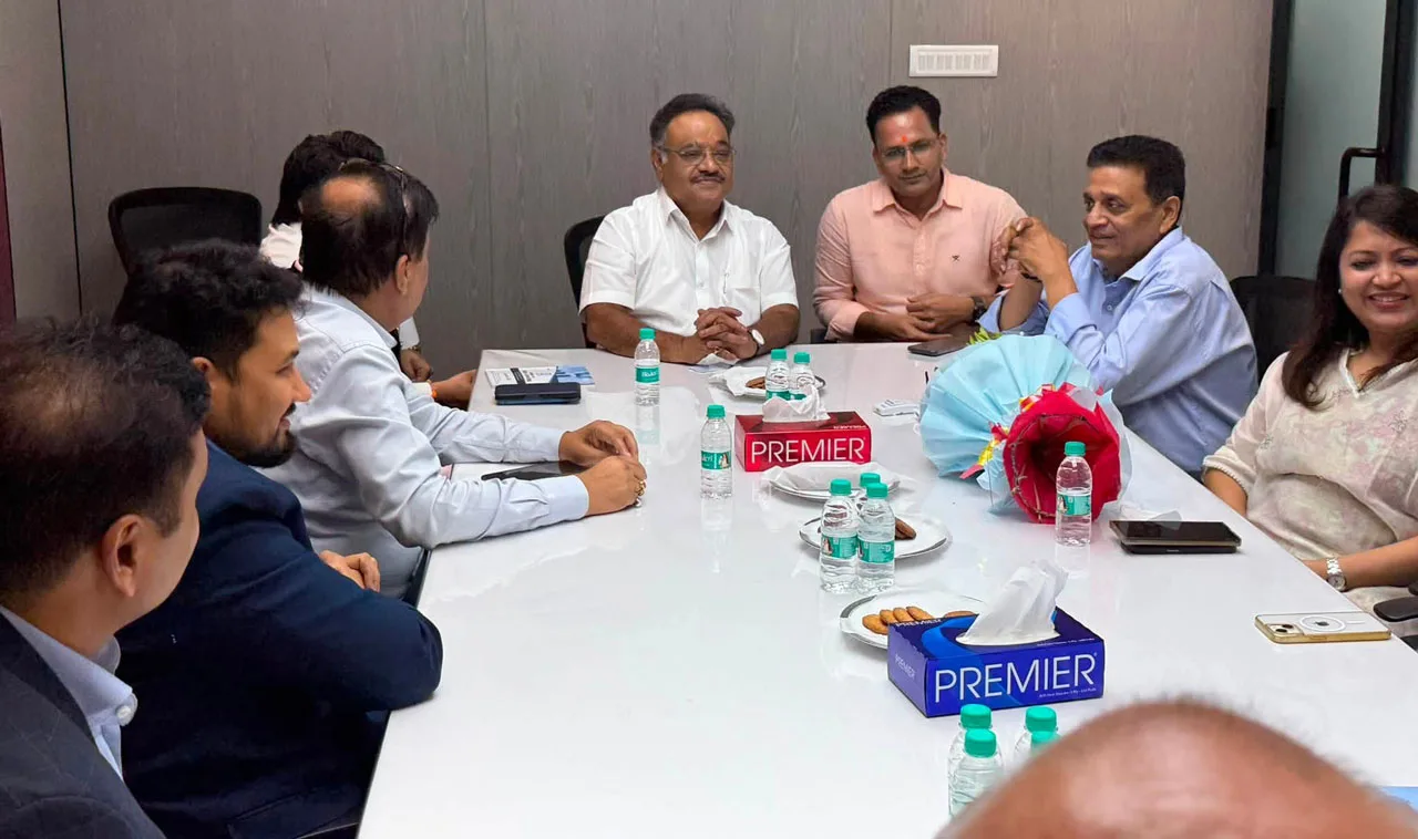 Group of professionals seated around a white conference table, engaged in a meeting with water bottles and snacks nearby.